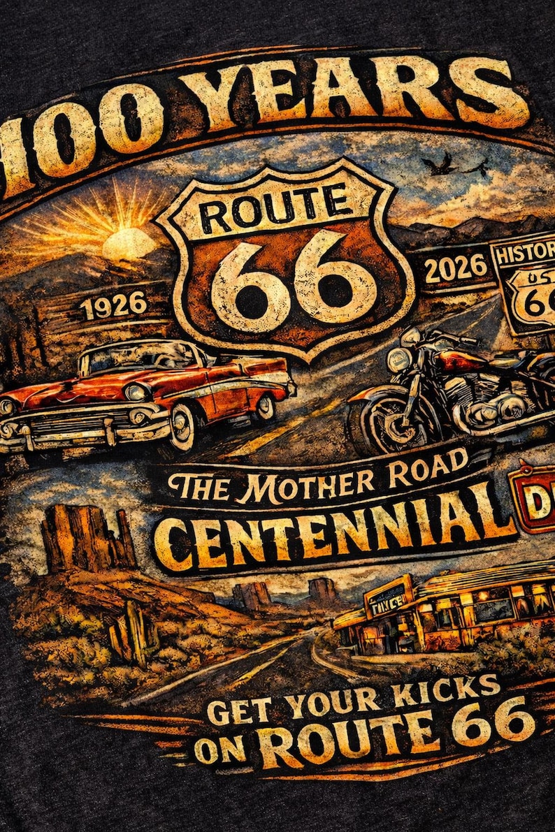 May include: A dark gray t-shirt featuring a graphic print of Route 66. The design includes a classic red car, a motorcycle, a desert landscape, and text reading 100 YEARS, ROUTE 66, 1926, 2026, THE MOTHER ROAD, CENTENNIAL, and GET YOUR KICKS ON ROUTE 66.