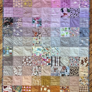 May include: A patchwork quilt featuring a range of colourful fabrics in shades of pink, purple, brown and orange. The quilt is composed of squares with different patterns and textures, resulting in a visually appealing and distinctive design.