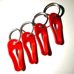 May include: Four red keychains with silver key rings. Each keychain has a unique shape with a curved design. The keychains are arranged diagonally against a white background, casting shadows.