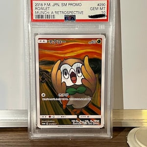 Peut inclure: Carte Pokémon gradée représentant Rowlet dans une parodie du "Cri" d'Edvard Munch. La carte est dans un étui de protection avec du texte indiquant qu'il s'agit d'une promo japonaise SM 2018. L'œuvre représente Rowlet avec ses mains sur son visage, imitant le tableau emblématique.