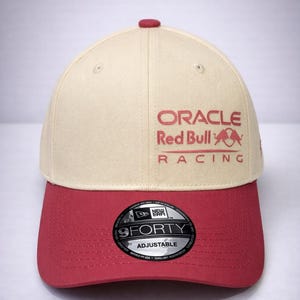 Puede incluir: Gorra de béisbol beige y roja con el texto "ORACLE Red Bull RACING". La gorra tiene una visera curva y una correa ajustable. El logotipo de New Era 9FORTY es visible.