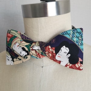 Puede incluir: Una pajarita estampada con un diseño de arte japonés. La pajarita tiene un patrón repetido de figuras en una variedad de colores, incluyendo rojo, azul, verde y beige. La pajarita se muestra en un maniquí.