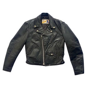 May include: Black leather motorcycle jacket with a silver zipper, two front pockets, and a small pocket on the chest. The jacket has a classic biker style with a notched collar and shoulder epaulets.