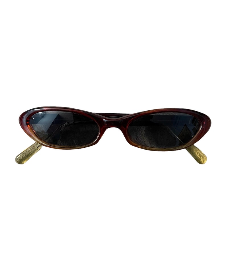Pu&ograve; includere: Occhiali da sole ovali marroni con lenti scure. La montatura passa da un marrone scuro a un marrone pi&ugrave; chiaro. Le aste sono di colore oro chiaro. Questi occhiali da sole sono un accessorio elegante.