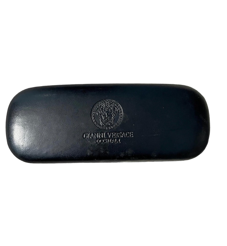 Pu&ograve; includere: Astuccio rettangolare nero per occhiali con la scritta in rilievo "GIANNI VERSACE OCCHIALI" e un emblema circolare. L'emblema presenta un disegno a testa di Medusa. L'astuccio &egrave; realizzato in un materiale liscio, possibilmente simile alla pelle.