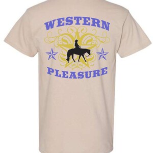 May include: Tan t-shirt with a Western-themed design. The back of the shirt features the words "WESTERN PLEASURE" in blue, with a silhouette of a rider on a horse, a yellow star, and blue stars.