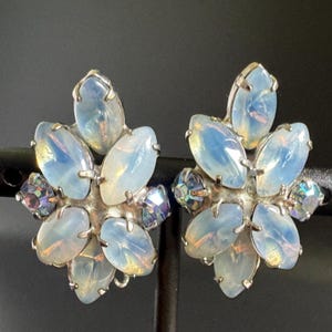 May include: A pair of silver-tone cluster earrings featuring marquise-cut, milky white opalescent cabochons arranged in a floral pattern, accented by small, iridescent, multi-colored faceted crystals on the outer edges of each earring.