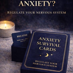 Puede incluir: Un juego de tarjetas "Anxiety Survival Cards" en una caja azul marino con letras doradas y un diseño de luna creciente y estrellas. El juego incluye una caja de tarjetas y una sola tarjeta que dice "Respira". El texto "¿Atrapado en la ansiedad paralizante?" está en la parte superior.