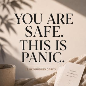 Peut inclure: Un jeu de 15 cartes d'ancrage avec le texte YOU ARE SAFE. THIS IS PANIC. 15 GROUNDING CARDS. La carte du dessus affiche le texte BREATHE. YOU ARE HERE. YOU ARE OKAY. avec une petite icône de cœur. Une tasse en céramique tachetée est visible.