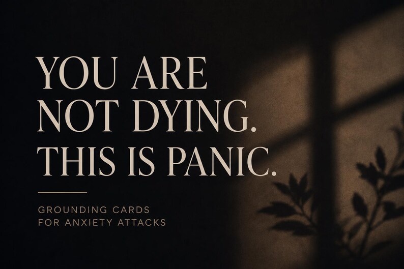 May include: A dark rectangular card featuring the beige text YOU ARE NOT DYING. THIS IS PANIC. followed by a horizontal line and the smaller text GROUNDING CARDS FOR ANXIETY ATTACKS. The right side shows a soft shadow of a plant against a dark background.