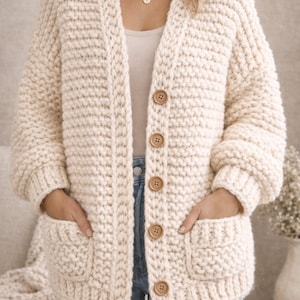 May include: Cream-colored, chunky knit cardigan with large wooden buttons and two front pockets. The open-front sweater has a relaxed fit and is made of a thick, textured yarn. The cardigan is a cozy, warm garment.