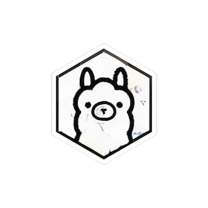 Może przedstawiać: Biała naklejka z czarnym obrysem kreskówki lamy wewnątrz białego sześciokąta. Lama ma okrągłą twarz, małe uszy i okrągły nos. Naklejka ma lekko postarzany, teksturowany wygląd.