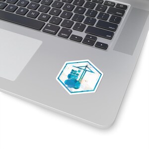 May include: A hexagonal sticker with a watercolour design of a crane and building. The sticker has a white border and a blue, white, and grey colour scheme. The sticker is placed on a laptop.