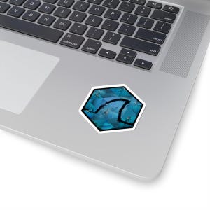 May include: A hexagonal sticker with a blue geometric design and a black outline of a shark fin. The sticker is on a laptop.