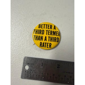 Könnte beinhalten: Ein runder gelber Ansteckbutton mit schwarzem Text, der BETTER A THIRD TERMER THAN A THIRD RATER lautet. Der Button liegt neben einem Metalllineal, das einen Durchmesser von etwa 4,5 Zentimetern für den runden politischen Anstecker zeigt.