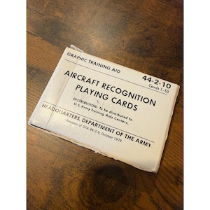 May include: A white card deck titled "Aircraft Recognition Playing Cards" with the text "Graphic Training Aid" and "Headquarters, Department of the Army." The deck is labeled 44-2-10, Cards 1-53.