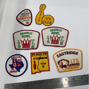 Könnte beinhalten: Eine Sammlung von sieben bestickten Bowling-Aufnähern in verschiedenen Formen und Farben, mit Texten wie WIBC League Champion 1962-83, Amarillo Bowl 175 Club und Eastridge 175 Award, platziert über einem Metalllineal mit einer Länge von 25 cm.