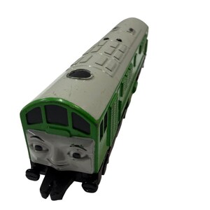 Könnte beinhalten: Eine grüne und graue Spielzeugeisenbahn mit einem geformten Gesicht auf der Vorderseite, das bemalte Augen und ein Lächeln aufweist. Die Oberseite ist grau mit rechteckigen Gitterdetails, während die Seiten grün sind und schwarze Räder zeigen.