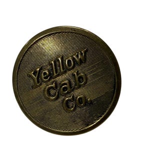 Pode incluir: Uma ficha metálica circular de cor latão com um fundo texturizado de linhas diagonais finas. As letras em relevo no centro dizem Yellow Cab Co. numa fonte serifada em negrito. O objeto tem uma borda exterior lisa e elevada.
