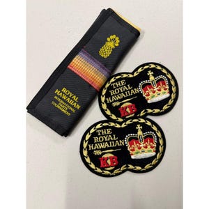 May include: Black fabric item with a pineapple and text "Royal Hawaiian International Darts Tournament". Two black patches with gold trim, a crown, and text "The Royal Hawaiian".
