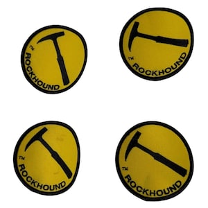May include: Four circular embroidered patches with a yellow background and a black border. Each patch features a black graphic of a rock hammer and the text ROCKHOUND printed in black along the bottom curve, accompanied by a small TM symbol.