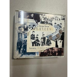 May include: A CD case featuring a collage of images of The Beatles. The album cover has a torn paper effect, with the band's name prominently displayed. The text "Recorded by THE BEATLES Hamburg" is visible.