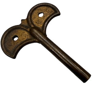 May include: A dark bronze-toned metal winding key featuring a T-shaped handle with two circular cutouts. The handle has a curved, wing-like design on both sides, and the shaft is a straight, solid cylinder extending from the center.