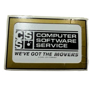 Puede incluir: Una pegatina rectangular con borde dorado y centro blanco. Presenta el texto negro CS COMPUTER SOFTWARE SERVICE, la frase WE'VE GOT THE MOVERS y el texto más pequeño A CHAS. LEVY COMPANY. El diseño incluye un logotipo estilizado.