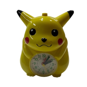Könnte beinhalten: Eine gelbe, Pikachu-förmige Analog-Uhr mit schwarz gespitzten Ohren, roten Wangen und großen schwarzen Augen. Das Zifferblatt befindet sich auf dem Bauchbereich und zeigt grüne Zahlen von 1 bis 12, einen roten Sekundenzeiger sowie schwarze Zeiger.