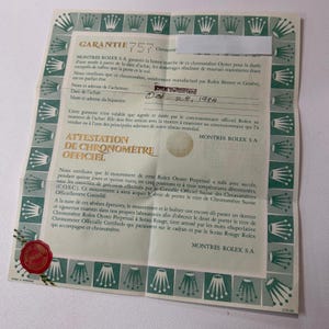Könnte beinhalten: Ein vintage Rolex Garantie- und offizielles Chronometer-Zertifikat auf hellgrünem Papier mit einem dunkelgrünen Rand aus wiederkehrenden Kronen-Logos. Das Dokument enthält den Text GARANTIE, ATTESTATION DE CHRONOMETRE OFFICIEL und ein rotes Wachssiegel in der unteren linken Ecke. Das Datum 28. Okt. 1984 ist handschriftlich in schwarzer Tinte vermerkt.