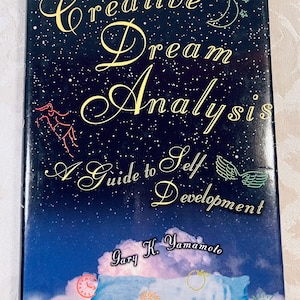 May include: A book titled "Creative Dream Analysis: A Guide to Self Development" with a dark blue cover featuring gold lettering and celestial illustrations. The author's name, Gary K. Yamamoto, is also visible.