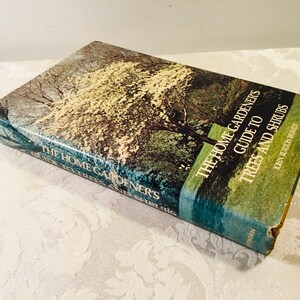 May include: A green and blue book titled "The Home Gardener's Guide to Trees and Shrubs" by John Burton Bruer. The cover features a photo of a tree with white blossoms.
