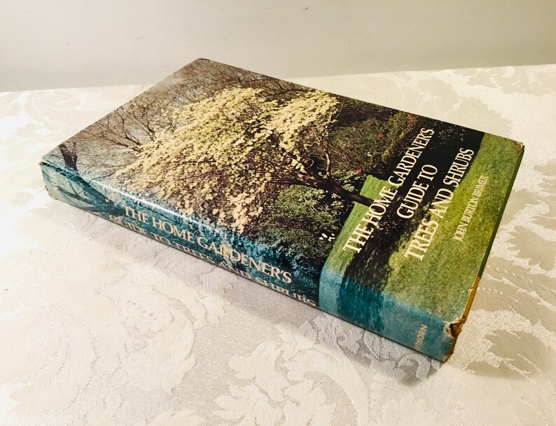 May include: A green and blue book titled "The Home Gardener's Guide to Trees and Shrubs" by John Burton Bruer. The cover features a photo of a tree with white blossoms.