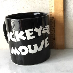 May include: Black ceramic coffee mug with white lettering that reads "Mickey Mouse".