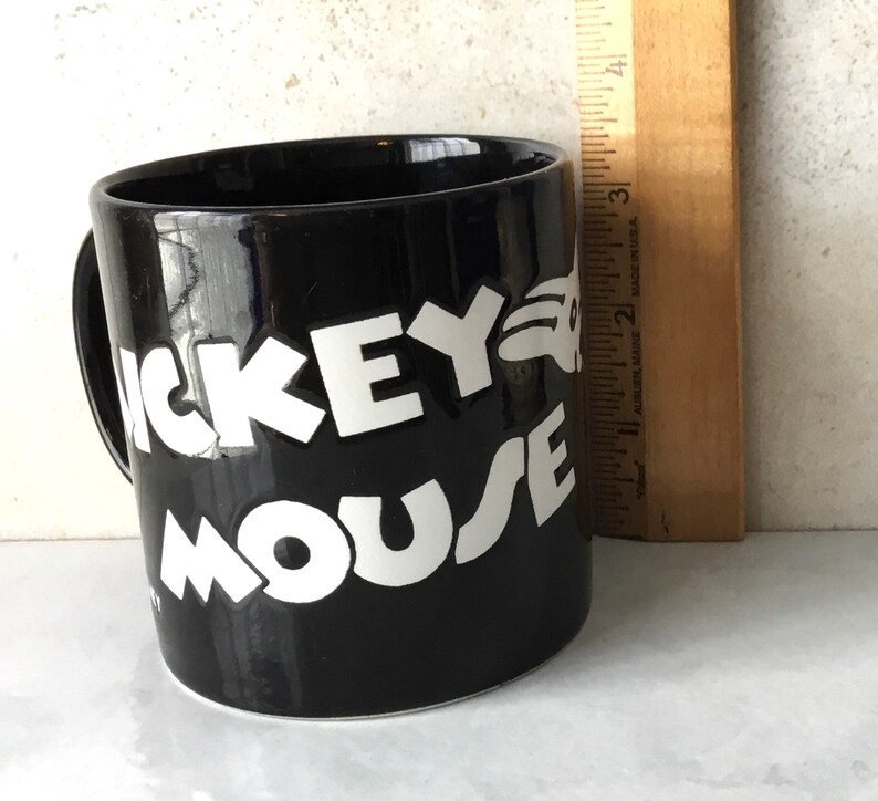 May include: Black ceramic coffee mug with white lettering that reads "Mickey Mouse".