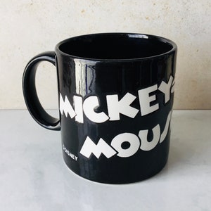 May include: Black ceramic mug with white lettering that reads "Mickey Mouse" and "Disney" at the bottom.