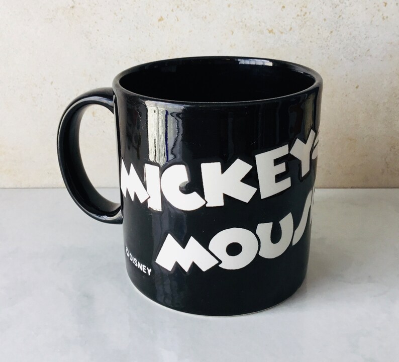 May include: Black ceramic mug with white lettering that reads "Mickey Mouse" and "Disney" at the bottom.