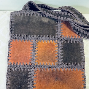 May include: A patchwork shoulder bag with a long strap. The bag is made of suede in shades of brown and orange, with each square stitched together with dark brown thread. The strap is also dark brown.