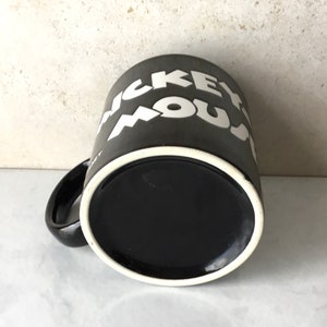 May include: Black ceramic coffee mug with white lettering that reads "Mickey Mouse".
