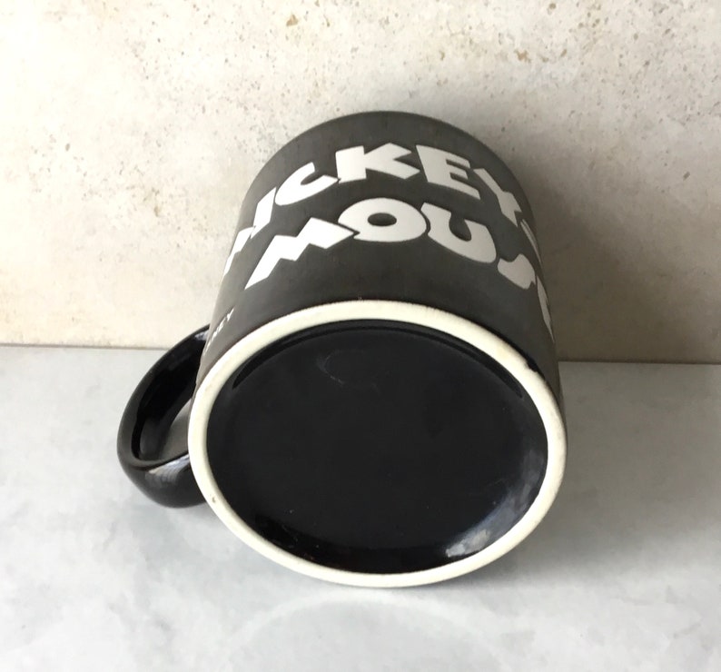 May include: Black ceramic coffee mug with white lettering that reads "Mickey Mouse".