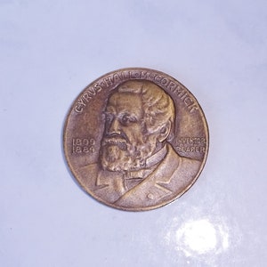 May include: A bronze coin with a portrait of Cyrus Hall McCormick, the inventor of the mechanical reaper. The coin reads "Cyrus Hall McCormick, Inventor of the Reaper, 1809-1884".