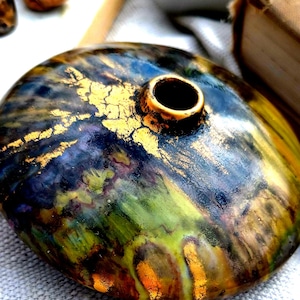 May include: A handcrafted, round ceramic vase with a small opening. The vase features a blend of colors, including blue, green, and gold, with a textured, crackled gold leaf design. The vase has a glossy finish.