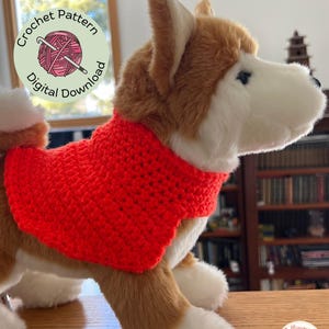 May include: A plush dog toy with brown and white fur, wearing a bright red crocheted sweater. The image includes text that reads "Jolligurumi Designs" and a circular graphic with the words "Crochet Pattern" and "Digital Download".