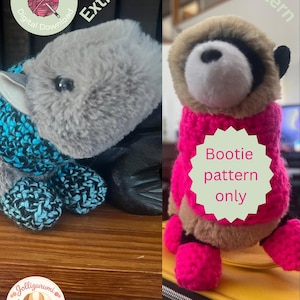 May include: Two crochet baby booties, one gray with blue accents and the other pink and brown. The image includes text that says "Extra Small Bootie Pattern" and "Bootie pattern only". A logo with a dog is also visible.