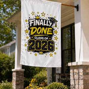 May include: A white graduation flag with the text "FINALLY DONE CLASS OF 2026" in black and yellow. The flag features a graduation cap graphic and star accents. The flag is hanging outside a house.