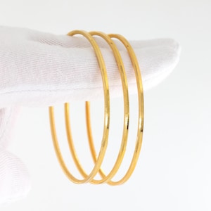 May include: Three thin, circular gold bangles with a textured, faceted surface. Each bangle features a consistent, polished yellow gold finish that reflects light along its rounded edges, creating a simple and uniform appearance for the set.