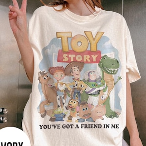 K&ouml;nnte beinhalten: Elfenbeinfarbenes T-Shirt mit dem Schriftzug "TOY STORY" und einer Grafik von Figuren aus dem Animationsfilm. Der Satz "YOU'VE GOT A FRIEND IN ME" ist darunter gedruckt. Das Shirt hat eine lockere Passform.