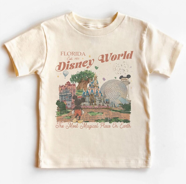 May include: Cream-colored t-shirt featuring a vintage-style illustration of Disney World in Florida. The design includes Mickey Mouse, the castle, and the text "Florida Disney World" and "The Most Magical Place On Earth."