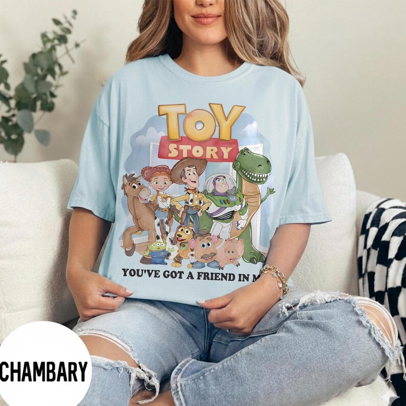 K&ouml;nnte beinhalten: Hellblaues T-Shirt mit den Worten "TOY STORY" in Gelb und Rot sowie einer Grafik von Figuren aus dem Film. Das Shirt hat auch den Text "YOU'VE GOT A FRIEND IN ME" in Schwarz.