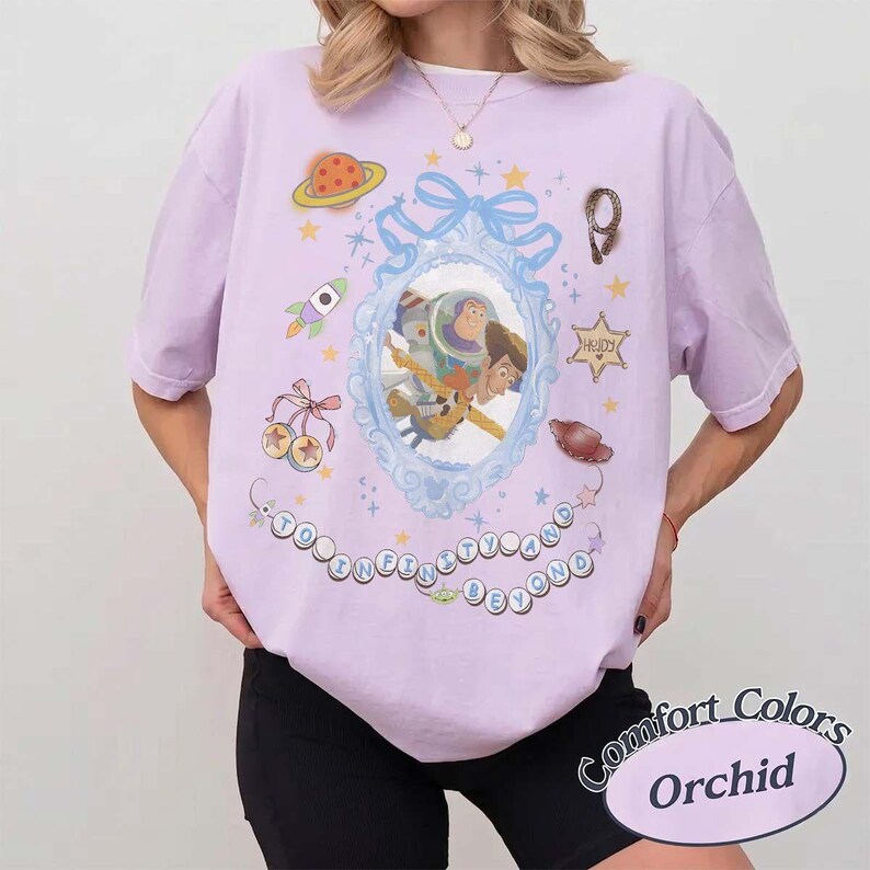 Peut inclure: Un t-shirt violet clair avec une impression graphique de Buzz l'&Eacute;clair et Woody dans un cadre bleu orn&eacute;. Le motif comprend une fus&eacute;e, une plan&egrave;te, une &eacute;toile de sh&eacute;rif avec le texte "Howdy" et le texte "To Infinity and Beyond" dans des cercles.